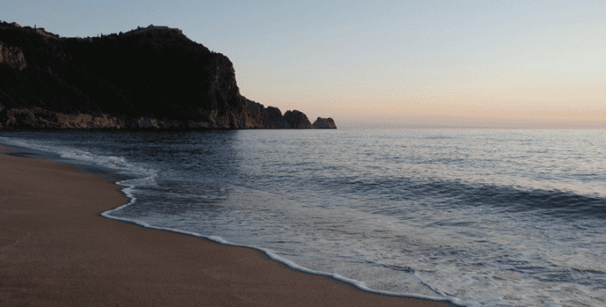 Plage sereine au coucher du soleil, falaise en arrière-plan.