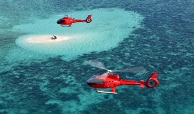 Location jet privé, hélicoptères survolant île sableuse et eau turquoise.