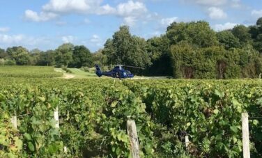 location de jet privé : Hélicoptère sur vignobles verdoyants et ciel partiellement nuageux.