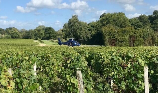 location de jet privé : Hélicoptère sur vignobles verdoyants et ciel partiellement nuageux.