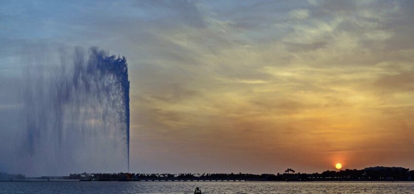 Un bateau solitaire au coucher du soleil avec fontaine et ciel orange.
