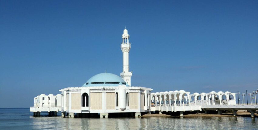 Mosquée blanche sur pilotis, dôme bleu, ciel clair.