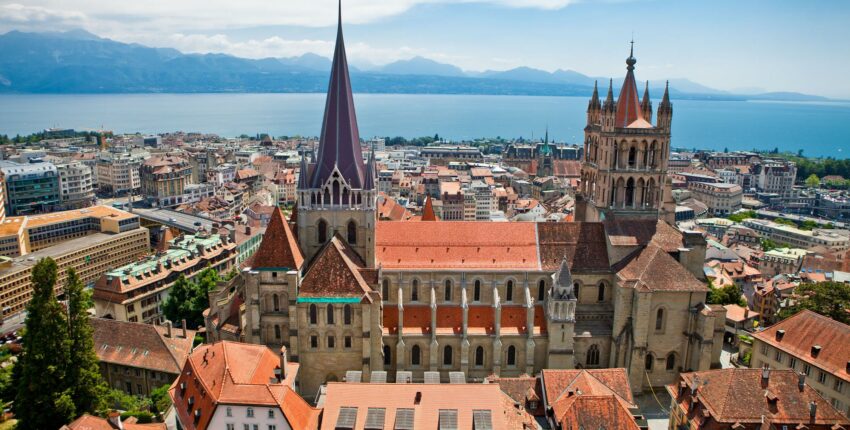 Vue aérienne Cathédrale de Lausanne, toits rouges, lac, montagnes.