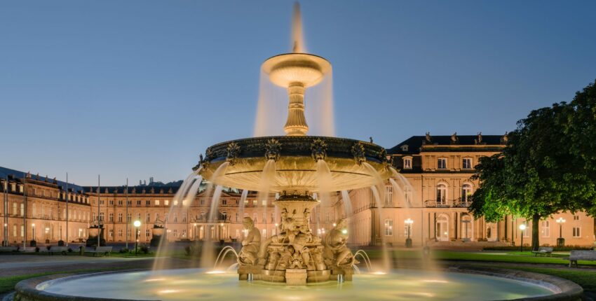 Fontaine éclairée devant bâtiment majestueux au crépuscule.