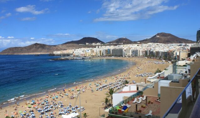 Las Palmas Gran Canaria plage bondée, eau bleue, montagnes.