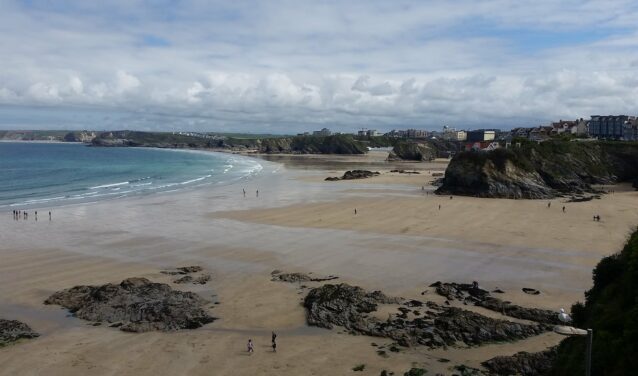 Plage Newquay, Cornouailles avec falaises rocheuses et bâtiments.