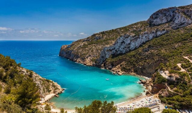 Plage isolée en Espagne entourée de falaises et de verdure.