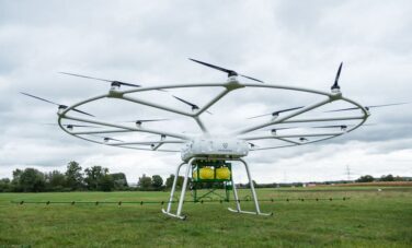 VOLODRONE survolant un champ herbeux sous ciel nuageux.