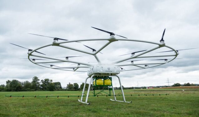 VOLODRONE survolant un champ herbeux sous ciel nuageux.